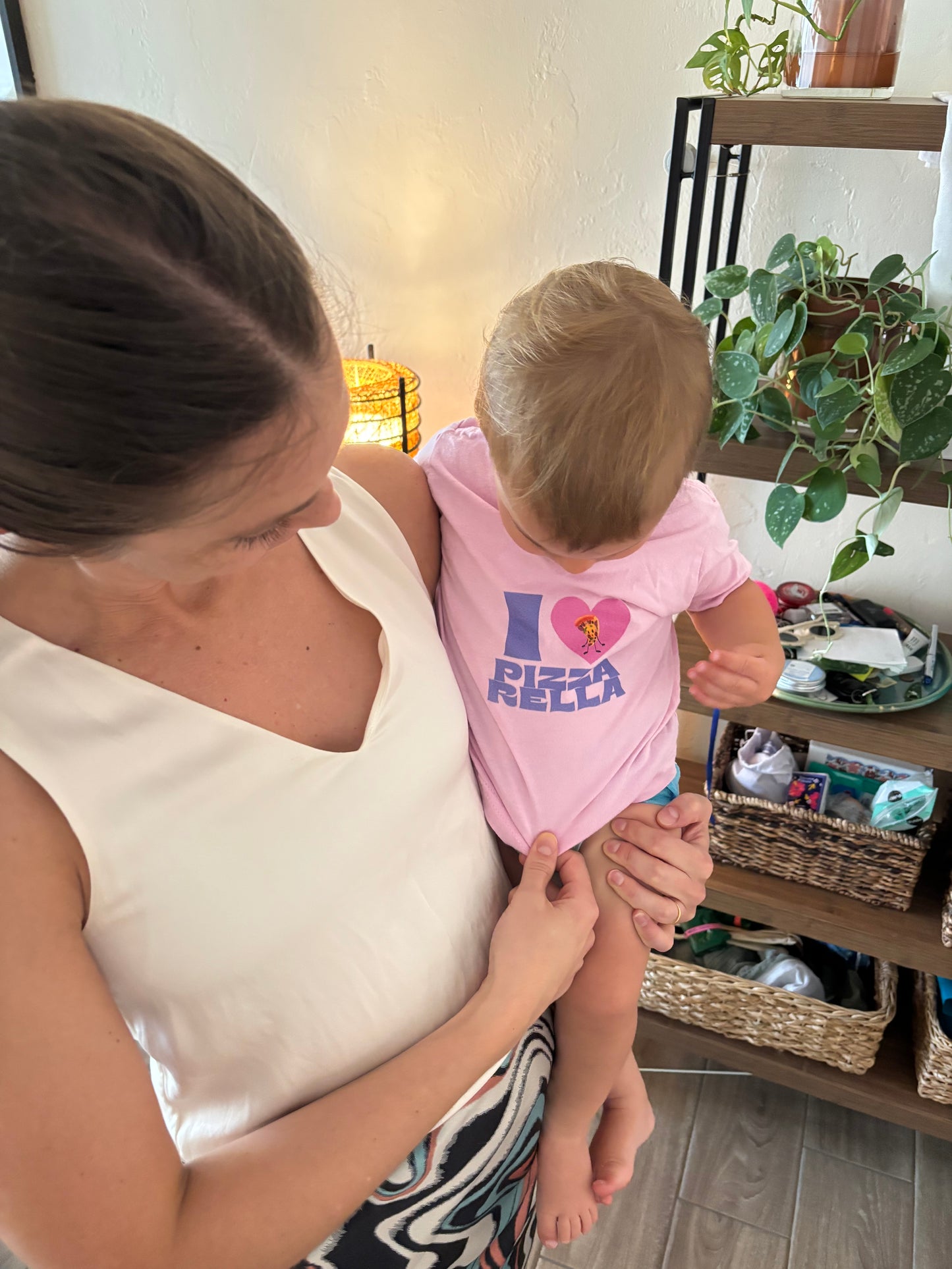 Woman holding a child wearing a pink shirt with text in a home setting