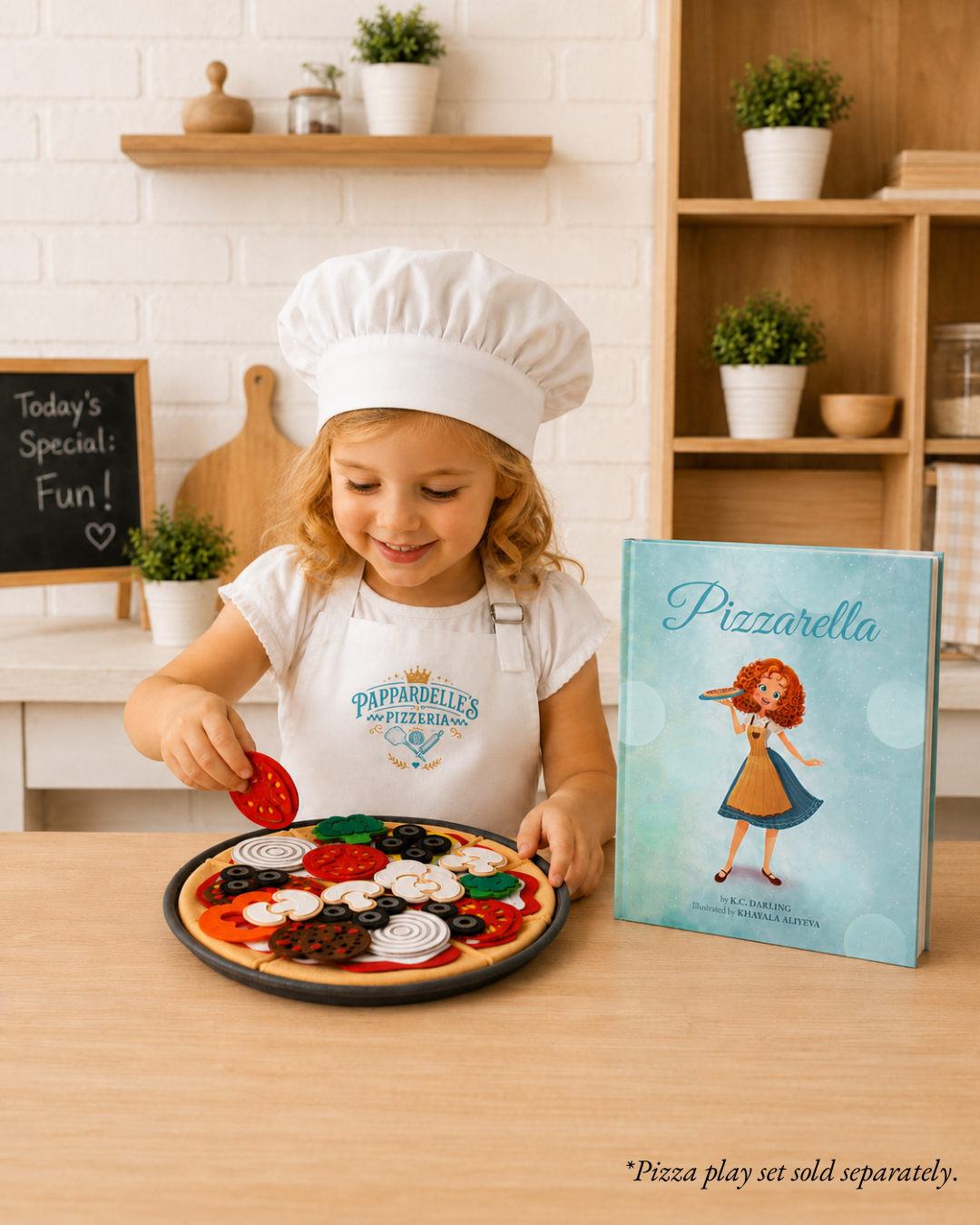 A young child wearing a white chef hat and white Pizzarella apron plays with a wooden Pizzarella pizza set on a light wood table, with the Pizzarella book standing next to them in a bright kitchen setting.